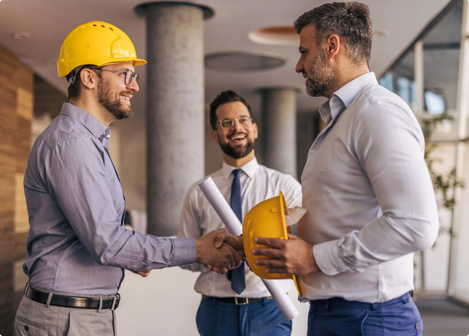 Three men shaking hands with hard hats.